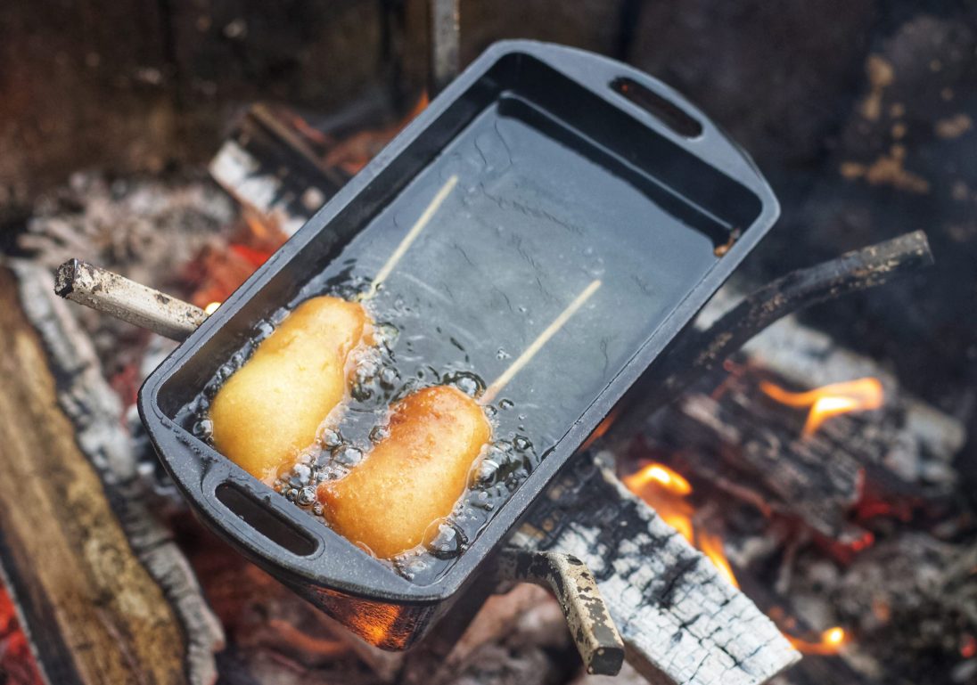 Corn dogs in pan over fire